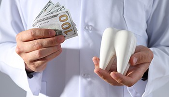 A dentist holding a model tooth and a few hundred-dollar bills