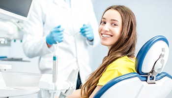 A woman with a toothy smile and a dentist in the background