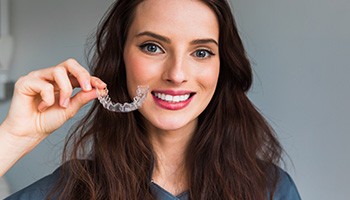 Woman smiling and holding an Invisalign aligner