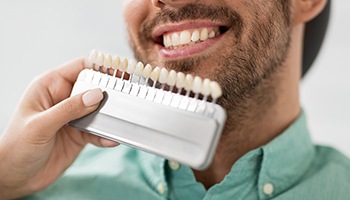 a smiling man having the color of his teeth matched by a dentist