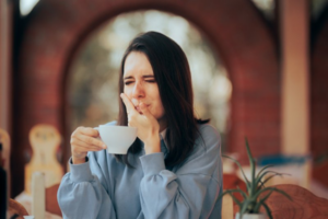 Woman at a coffee shop wincing because the heat hurts her tooth